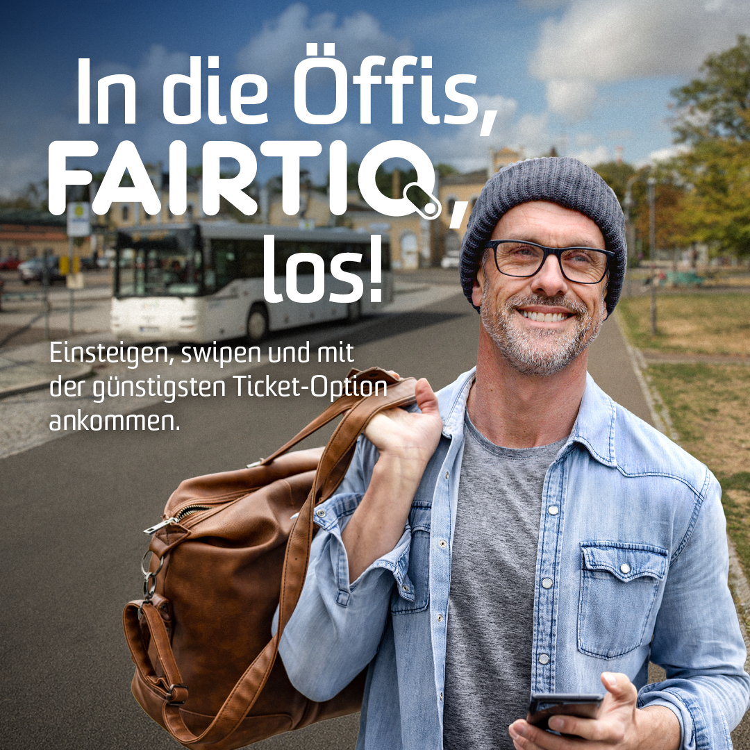 Mann mit Smartphone steht am Busbahnhof